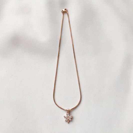 Lakx Fashion gold-toned chain necklace with a leaf-shaped pendant featuring clear white crystals on a silk background