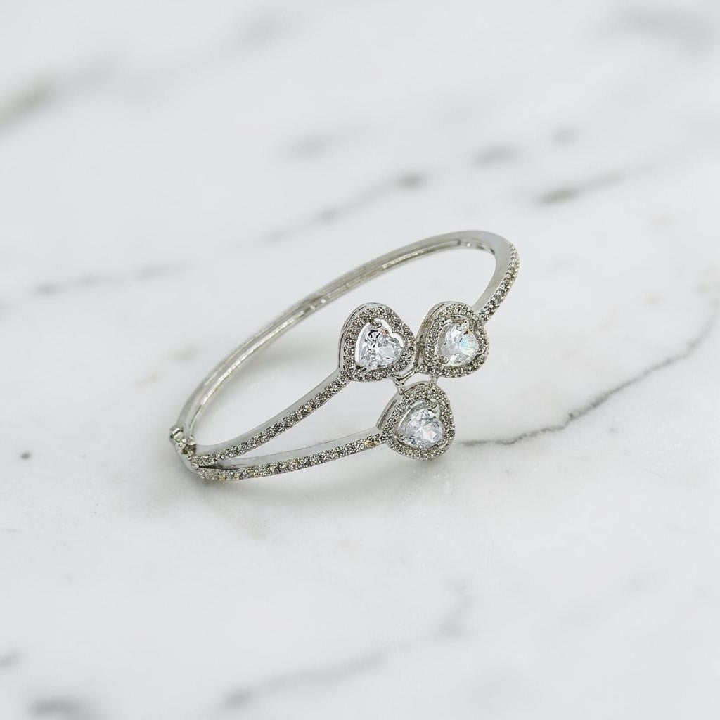 Lakx Fashion rhodium-tone brass hinged kada bracelet with three heart-shaped CZ stones and pavé-set halos.