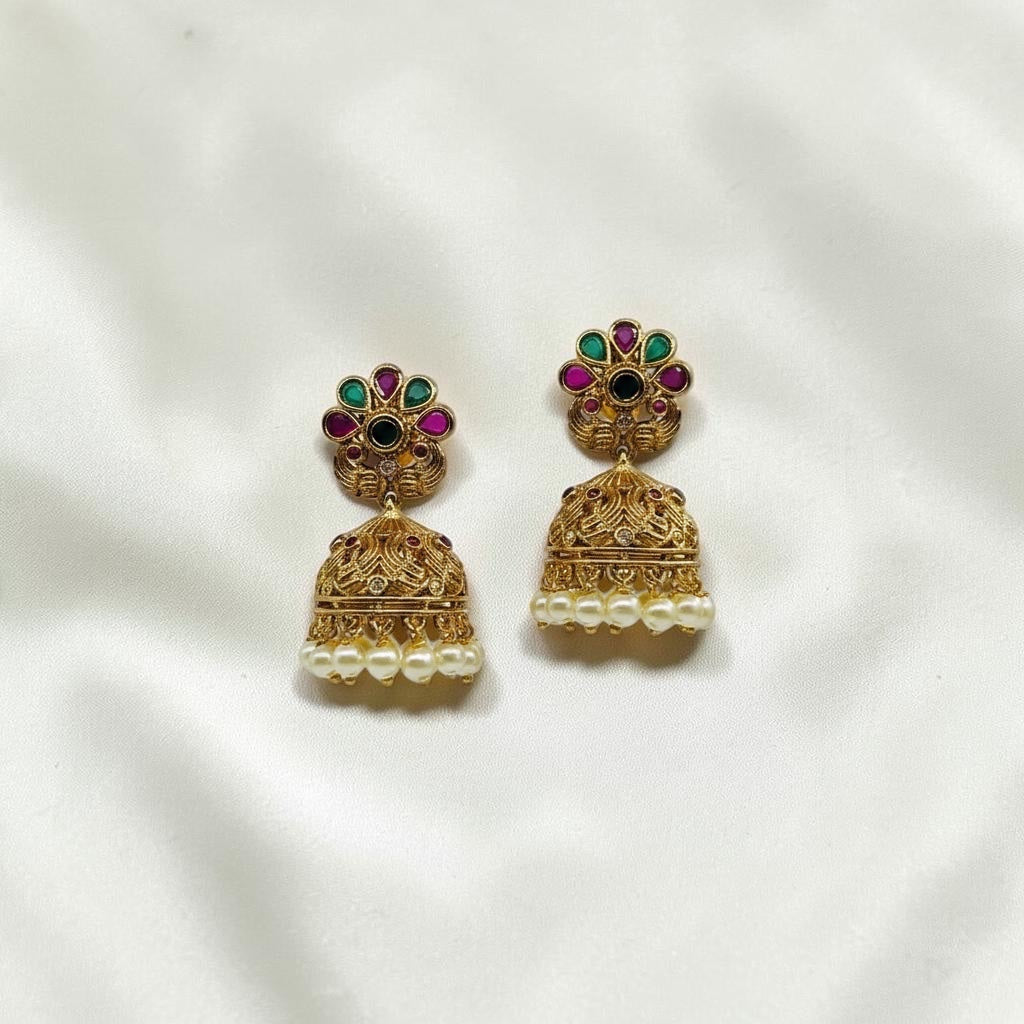 Lakx Fashion gold-tone brass jhumka earrings with floral studs, green and ruby stones, and dangling light yellow pearls.