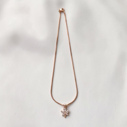 Lakx Fashion gold-toned chain necklace with a leaf-shaped pendant featuring clear white crystals on a silk background