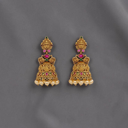 Lakx Fashion gold-tone brass jhumka earrings with temple motifs, red and green stones, and dangling yellow pearls.