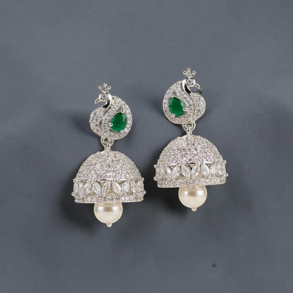 Lakx Fashion rhodium-tone jhumka earrings featuring peacock motifs, emerald green stones, diamonds, and pearl drops.