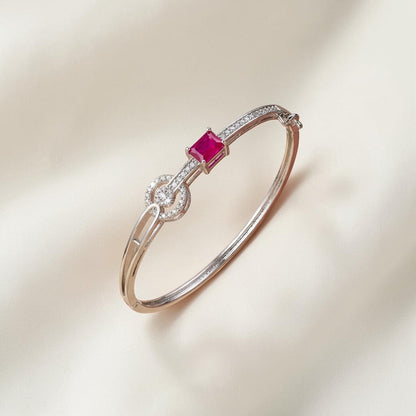Lakx Fashion rhodium-tone brass bangle featuring a vibrant emerald-cut red stone and sparkling white CZ accents.
