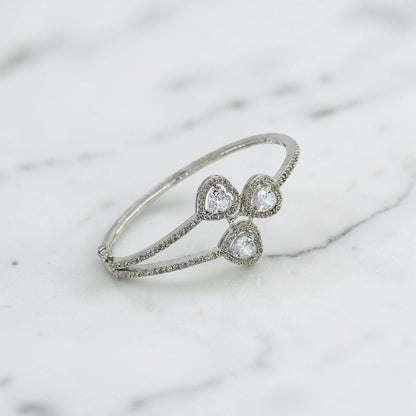 Lakx Fashion rhodium-tone brass hinged kada bracelet with three heart-shaped CZ stones and pavé-set halos.