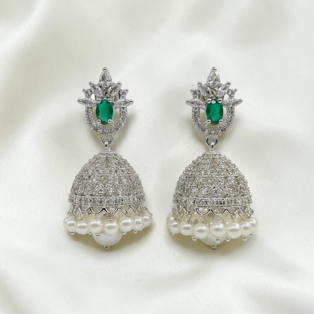 Lakx Fashion rhodium-tone jhumka earrings with green teardrop stones, white CZ, and pearl drops on a white silk background.