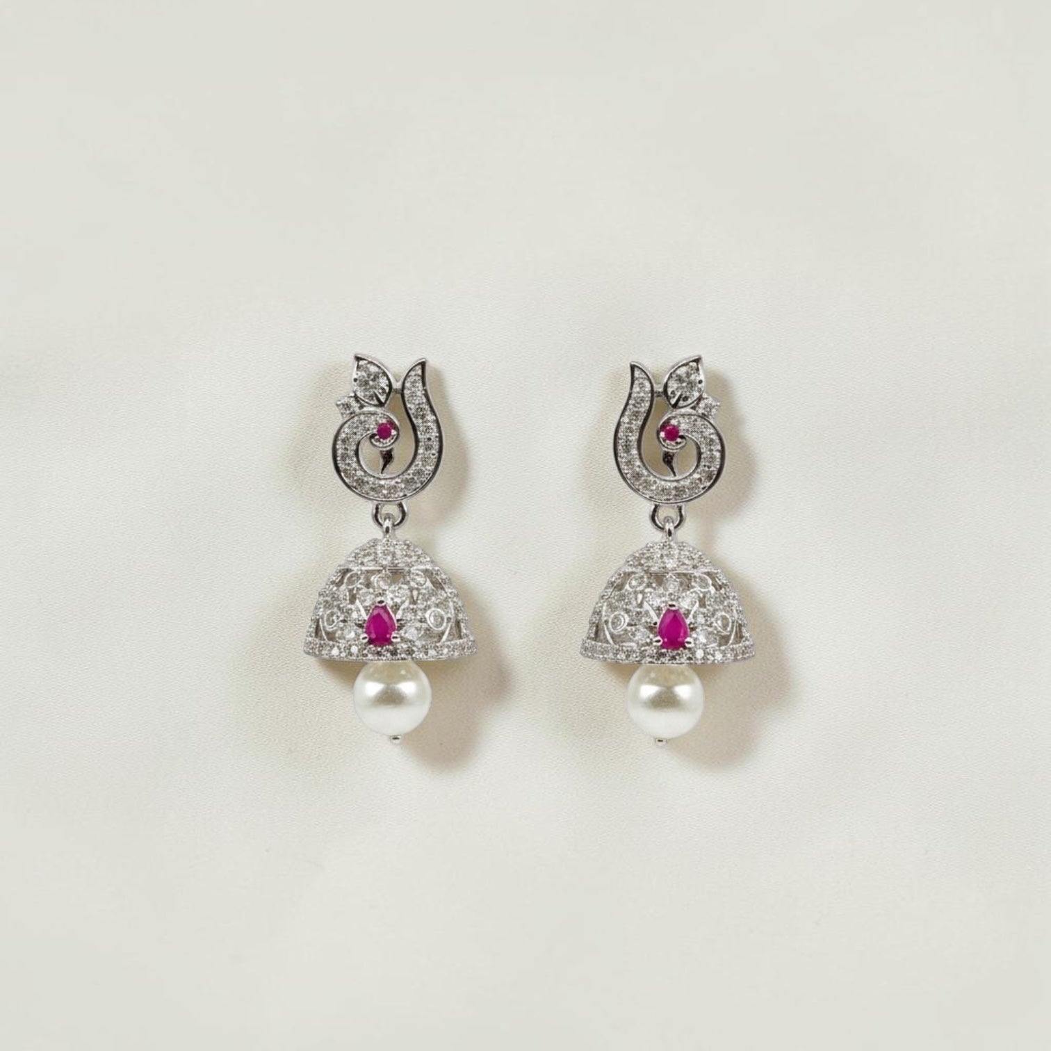 Lakx Fashion rhodium-tone jhumka earrings with peacock motif, ruby-colored stones, white CZ, and pearl drops.