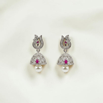 Lakx Fashion rhodium-tone jhumka earrings with ruby stones, white CZ, peacock motif, and pearl drops on white fabric.