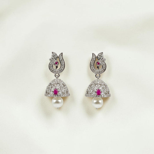 Lakx Fashion rhodium-tone jhumka earrings with ruby stones, white CZ, peacock motif, and pearl drops on white fabric.
