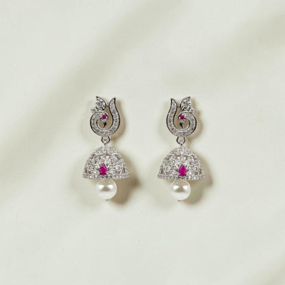 Lakx Fashion rhodium-tone brass jhumka earrings with ruby-colored stones, white CZ, and pearl drops on wood background.
