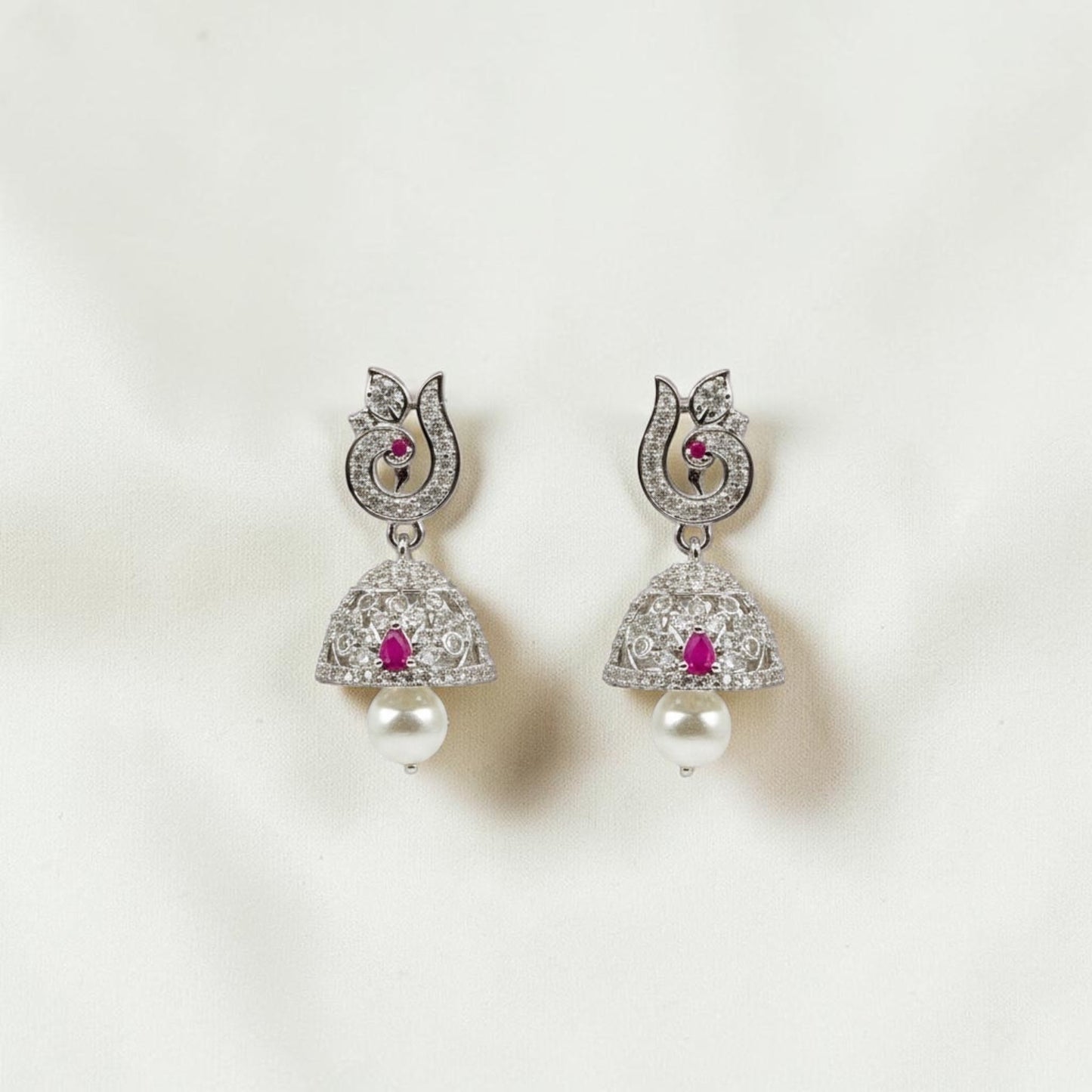Lakx Fashion rhodium-tone jhumka earrings with ruby-colored stones, white CZ, and pearl drops in a peacock design.