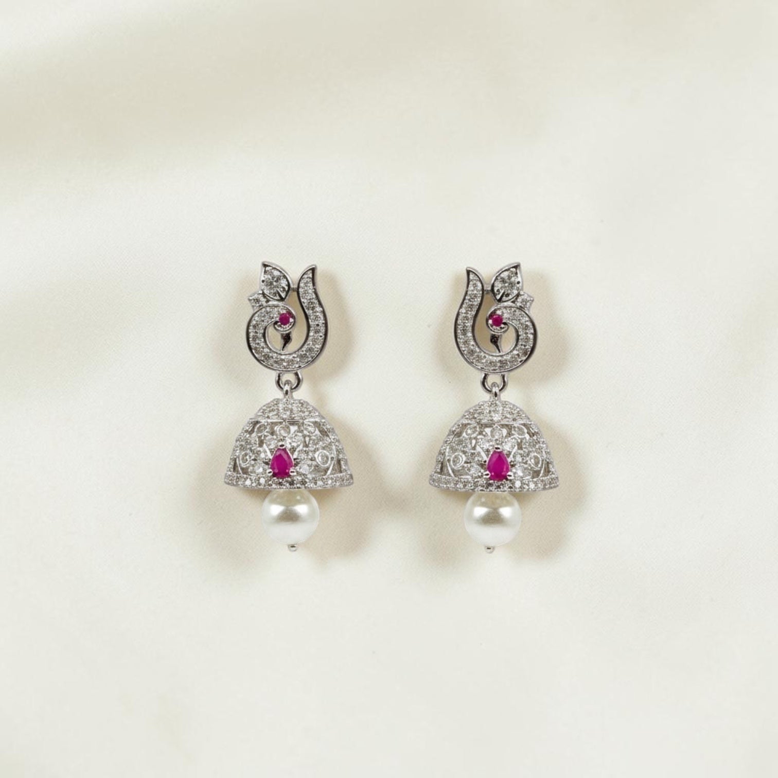 Lakx Fashion rhodium-tone jhumka earrings with peacock motifs, ruby-colored stones, white CZ, and pearl drops.